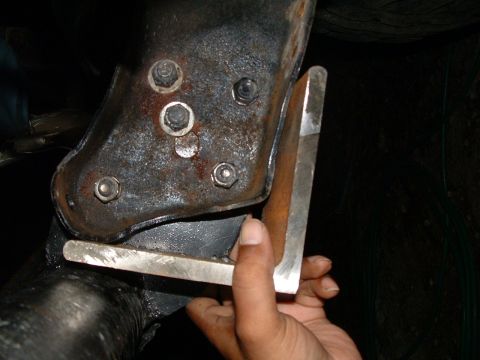 1979 Ford Bronco - Hand holding a metal bracket against a vehicle's frame, showing bolted connections.