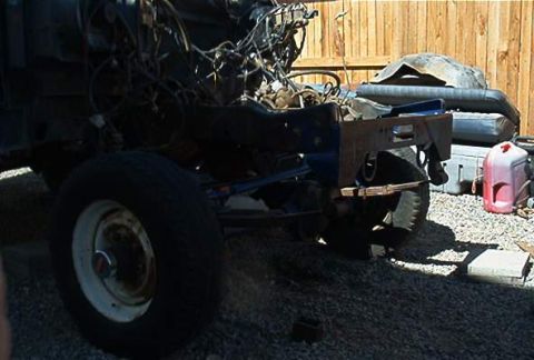1986 Ford Bronco - A partially disassembled vehicle chassis viewed from the front-left, with the front bodywork removed exposing the engine, wiring, and frame…
