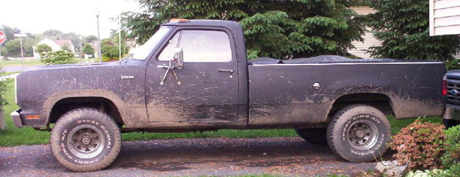 Side view of a mud-covered black Dodge pickup truck parked in a driveway