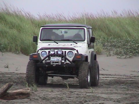 1994 Ford Explorer - A white Jeep Wrangler is parked on a sandy beach with tall grass in the background.