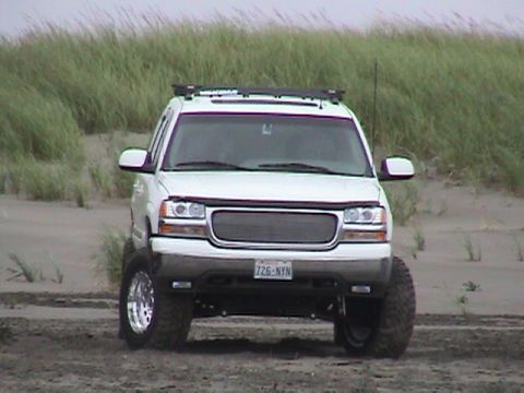 1994 Ford Explorer - This white SUV, likely a GMC Yukon or Chevrolet Tahoe from the early 2000s, is positioned on a sandy terrain with dunes and vegetation.