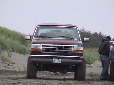 1994 Ford Explorer - A maroon Ford Bronco is parked on a sandy beach with dunes and trees in the background.