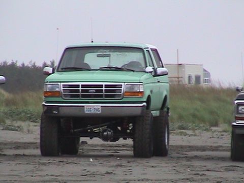 1994 Ford Explorer - A lifted green 1994 Ford Explorer is parked on a beach, with another vehicle visible to the right.