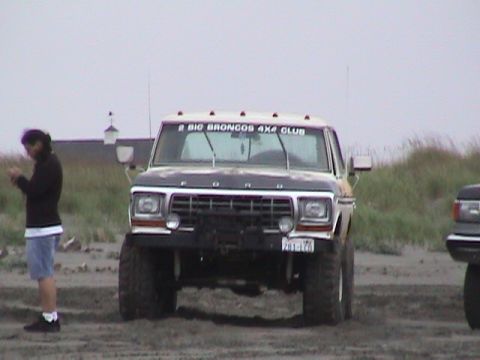1994 Ford Explorer - A lifted Ford pickup truck with off-road tires is parked on a sandy area, with another vehicle partially visible to the right.