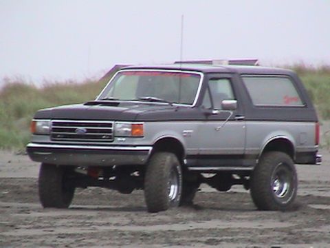 1994 Ford Explorer - A two-tone Ford Bronco is parked on a sandy terrain, viewed from the front-left angle.