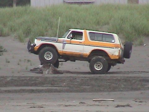 1994 Ford Explorer - A vintage Ford Bronco is positioned on a sandy beach, with its front tire resting on a piece of driftwood.