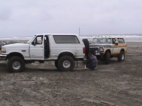 1994 Ford Explorer - A white 1994 Ford Bronco is parked on the beach with its door open, while a second Bronco is visible behind it.