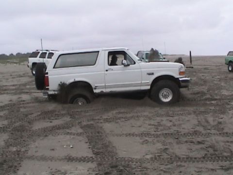 1994 Ford Explorer - White 1994 Ford Bronco stuck in sand on a beach, with another SUV visible in the background.