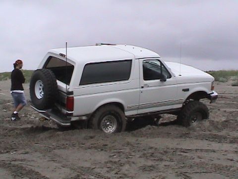 1994 Ford Explorer - A white Ford Bronco is stuck in the sand, with a person observing the situation.