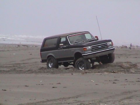1994 Ford Explorer - Ford Bronco stuck in the sand on a beach with the ocean in the background.