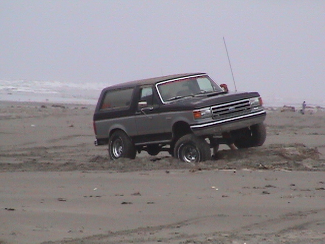 Two-tone Ford Bronco stuck in sand on a beach, front wheels buried