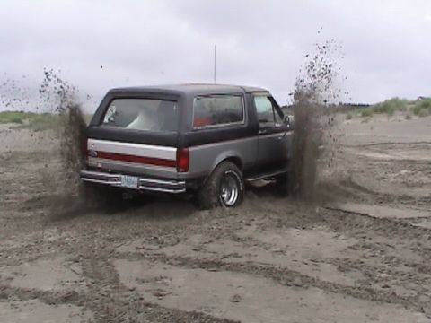 1994 Ford Explorer - A 1994 Ford Bronco drives through sand, kicking up dirt from its rear tires.