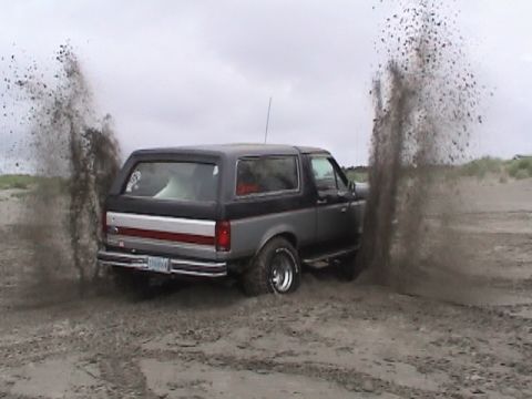 1994 Ford Explorer - Ford Bronco driving on a sandy terrain, kicking up large plumes of sand.