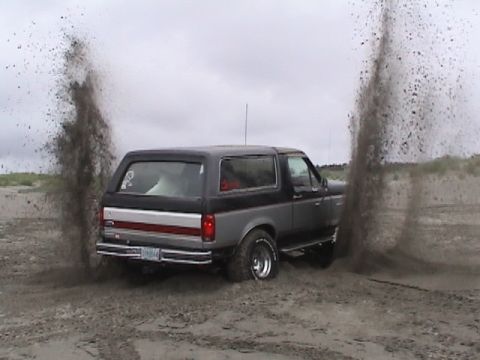 1994 Ford Explorer - A Ford Bronco is partially submerged in sand, with large plumes of dirt erupting around it.