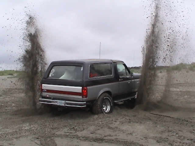 Gray Ford SUV spinning tires and throwing sand rooster tails on a beach