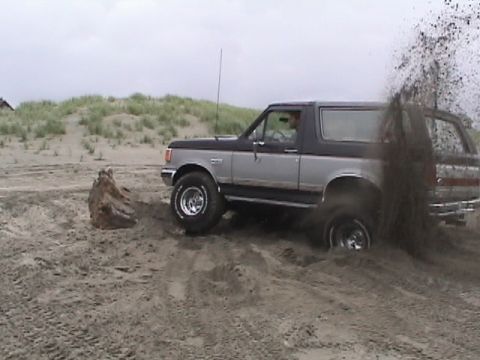 1994 Ford Explorer - A Ford Bronco navigates a sandy terrain, with sand spraying from its rear tires.