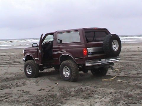 1994 Ford Explorer - A maroon Ford Bronco sits on a beach with its door open and a spare tire mounted on the rear.