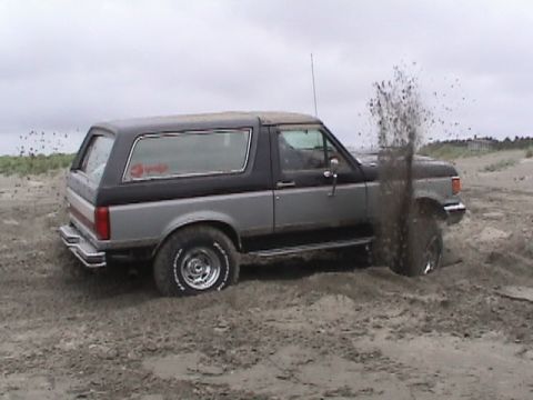 1994 Ford Explorer - Ford Bronco is stuck in the sand, with dirt spraying from the wheel.