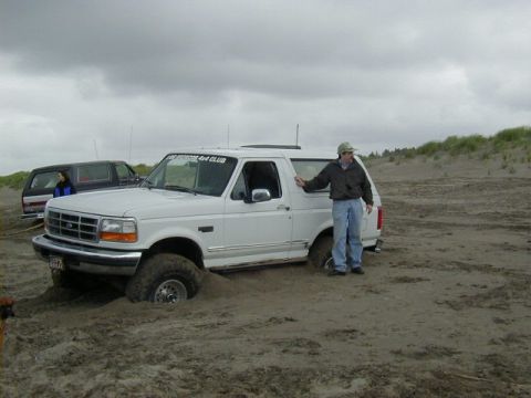1994 Ford Explorer - A white Ford Bronco is stuck in the sand, with a person standing beside it and another vehicle in the background.