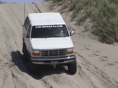 1994 Ford Explorer - White Ford Bronco navigates a sandy incline, displaying a club sticker on its windshield.
