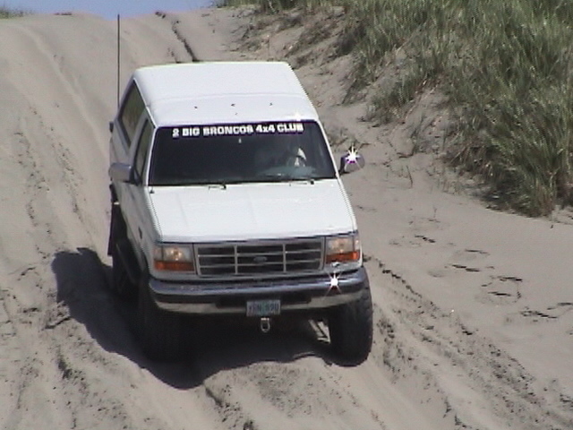 White lifted Ford Bronco climbing a sand dune with 2 Big Broncos 4x4 Club windshield banner