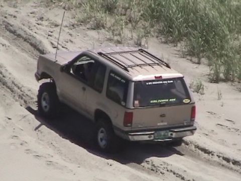 1994 Ford Explorer - A tan SUV with a roof rack and lifted suspension navigates sandy terrain.
