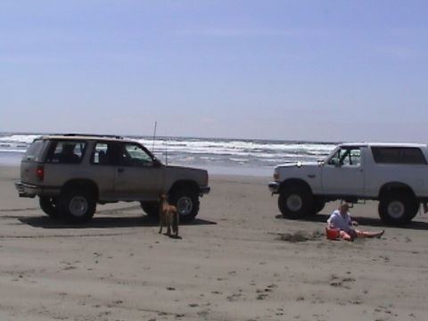1994 Ford Explorer - A tan 1994 Ford Explorer is parked on the beach next to a white SUV, with a person sitting in the sand.