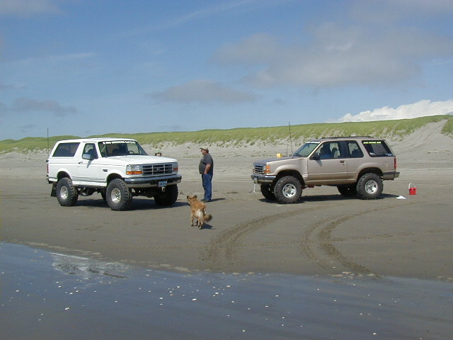 White lifted Ford Bronco and tan two-door Explorer parked on a sand beach with dunes