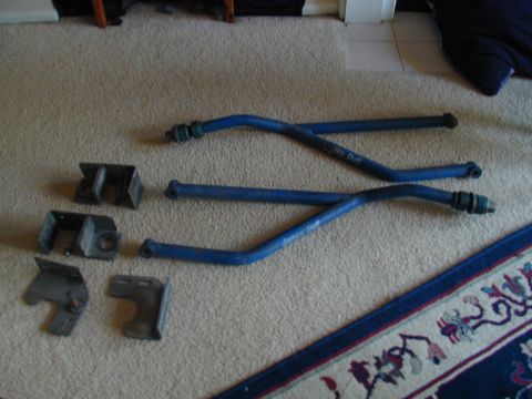 1988 Ford Bronco - Several blue suspension bars and metal brackets are laid out on a carpeted floor next to a rug.