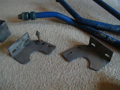 1988 Ford Bronco - Metal brackets and blue suspension bars are laid out on a carpeted surface.