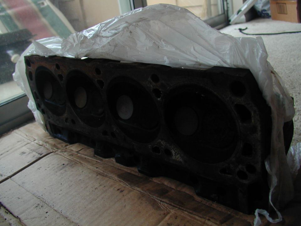 Black engine block covered in plastic, resting on cardboard