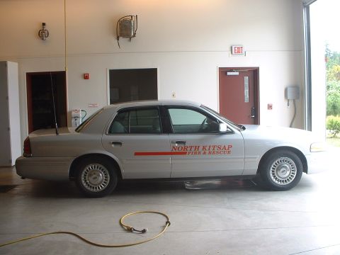 1999 Ford Crown Victoria - A silver Ford Crown Victoria, marked for North Kitsap Fire & Rescue, is parked indoors with a yellow hose on the floor.