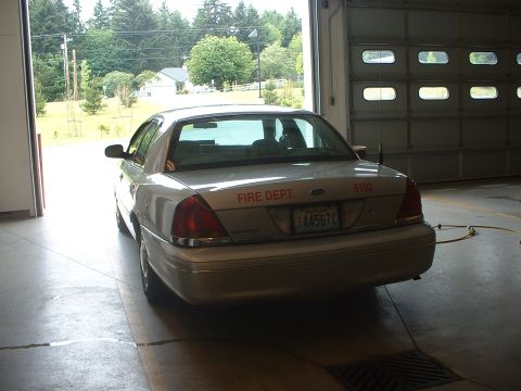 1999 Ford Crown Victoria - A Ford Crown Victoria, likely a police interceptor, is parked inside a garage with the bay door open.