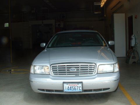 1999 Ford Crown Victoria - A silver 1999 Ford Crown Victoria is parked facing forward in a garage, displaying its front grille and Washington state license plate.