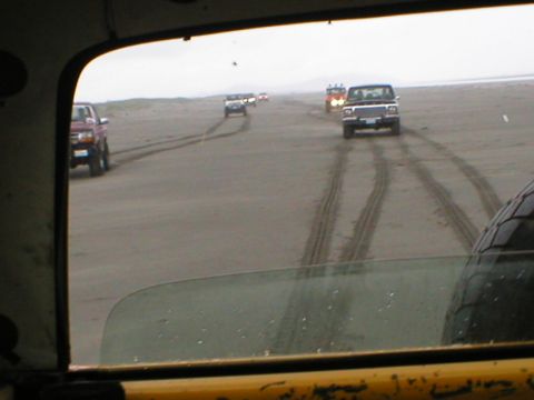 1978 Ford Bronco - A group of SUVs are seen driving on a sandy beach, creating tire tracks on the wet sand.