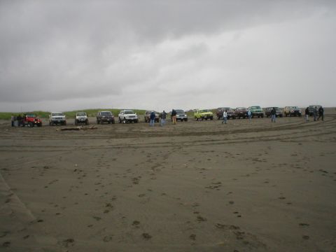 1978 Ford Bronco - Several SUVs and a red Jeep gathered on a beach, with people standing around them.
