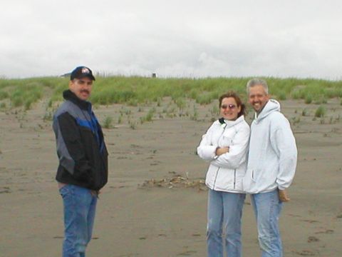 1978 Ford Bronco - Three people pose for a photo on a sandy beach with dunes and overcast skies in the background.