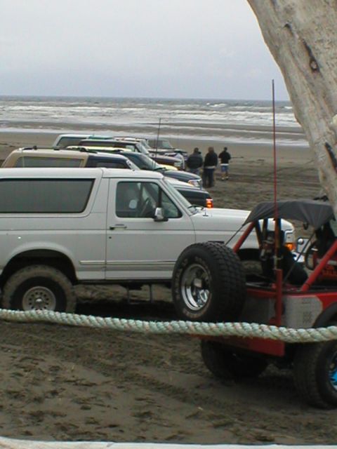 1978 Ford Bronco - Several vehicles are parked on the sand near the ocean, including a white Ford Bronco and a red dune buggy.