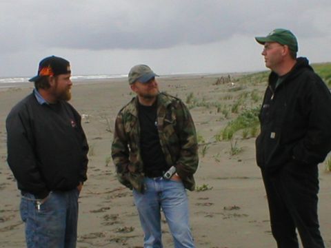 1978 Ford Bronco - Three men converse on a beach, with the ocean and dunes visible behind them.
