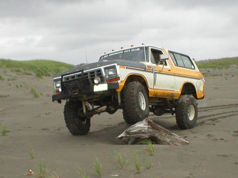 1978 Ford Bronco - This lifted 1978 Ford Bronco, sporting a "BIG BRONCOS 4X4 CLUB" sticker, navigates a sandy beach with a driftwood log nearby.