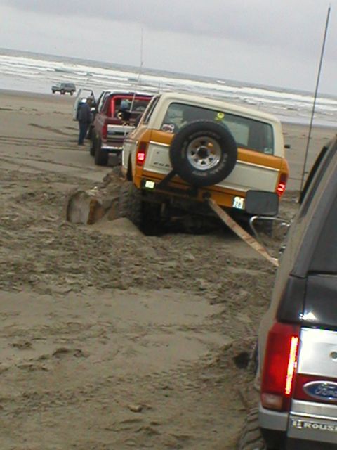 1978 Ford Bronco - Several vehicles are stuck in the sand on a beach, with one Bronco being towed.