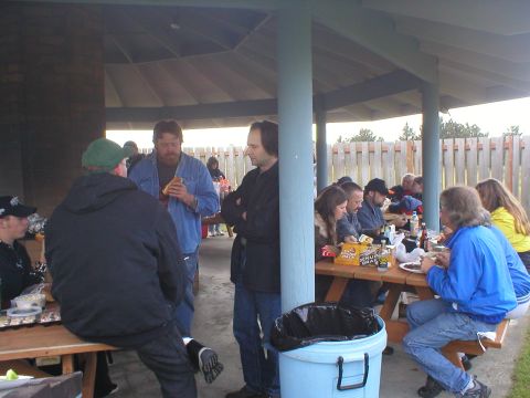1978 Ford Bronco - A group of people are gathered for a meal at picnic tables under a covered outdoor shelter.
