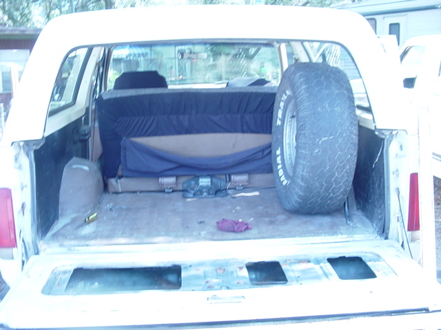 Interior cargo area of white SUV with spare tire and folded blue rear seat, viewed from open tailgate