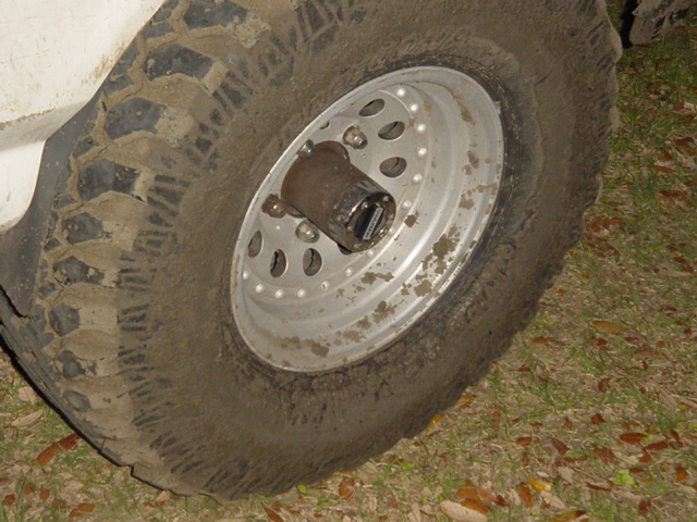 Muddy mud-terrain tire on white steel wheel with manual locking hub on a 4x4