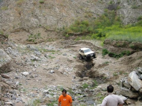 1985 Ford Bronco - A white SUV navigates a challenging off-road course through a rocky, uneven landscape.