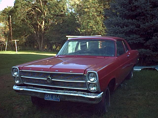 Red 1966 Ford Fairlane sedan, front three-quarter view, parked on grass with plate SKE 814