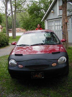 1997 Ford Taurus - This red sedan is wearing a car bra, parked outside a garage with a person peeking out.