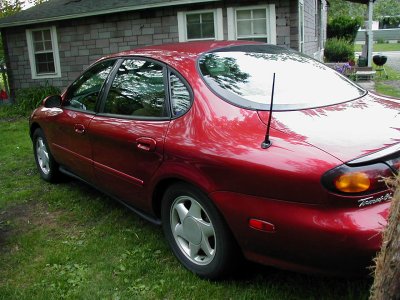 1997 Ford Taurus - Rear quarter view of a red 1997 Ford Taurus parked on a grassy lawn.