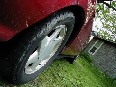 1997 Ford Taurus - A close-up view of a red car's wheel and fender, with a building in the background.