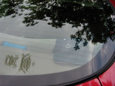 1997 Ford Taurus - A red car's rear window displays a Nike logo sticker, with tree reflections visible.